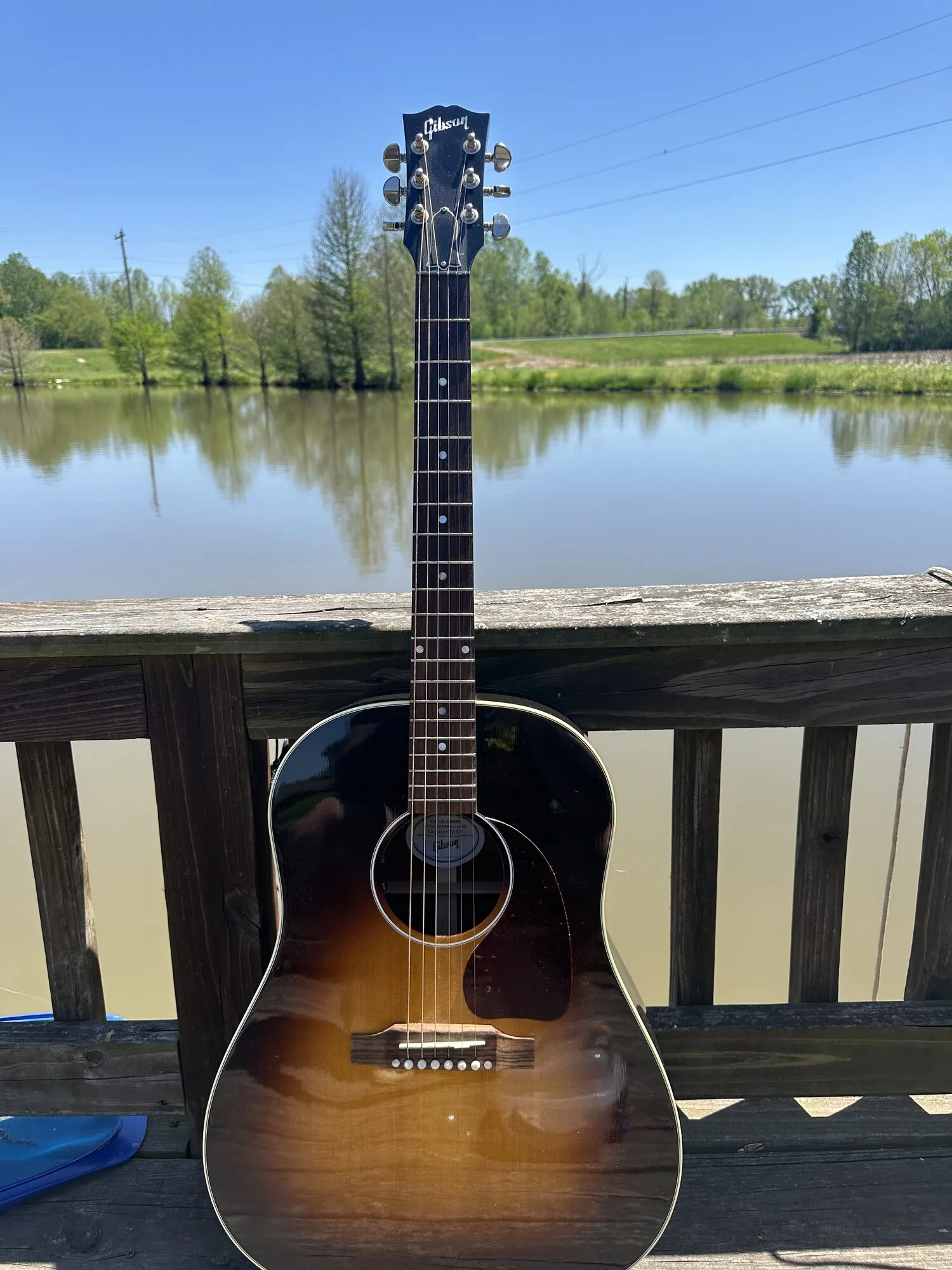An acoustic guitar on the dock, the pond and trees of the estate behind